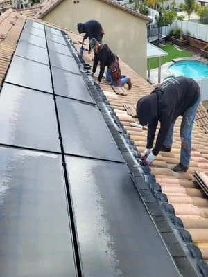 Two workers installing black solar panels on residential tile roof in Temecula