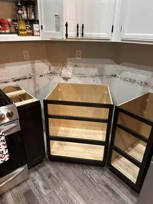 Black-framed glass cabinet doors with natural wood drawer fronts during kitchen cabinet installation