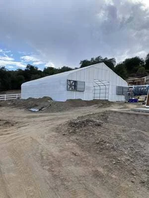 White metal agricultural building with arched roof under construction on prepared site