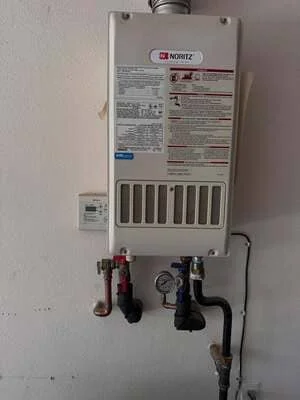 Installed Noritz tankless water heater with red and black shut-off valves on white wall