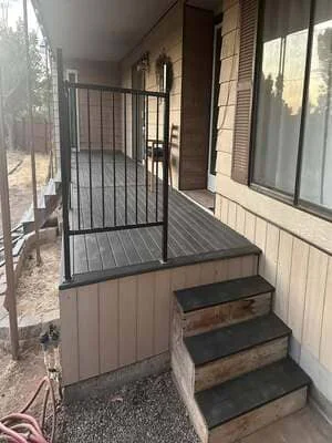 Residential entry deck with black composite decking, metal railing, and concrete steps with black treads