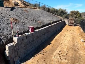 Stone retaining wall with gravel backfill on sloped hillside construction site