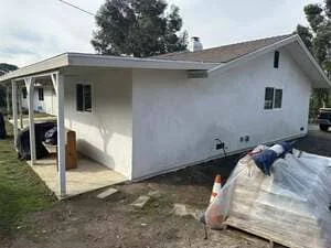 White stucco residential addition with covered porch and new construction framing visible