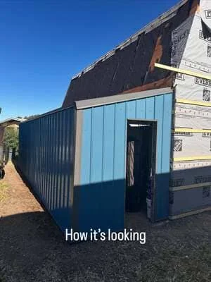 Blue metal storage shed with new corrugated siding and dark roof under clear sky