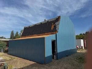 Blue and black metal building under construction with corrugated steel siding and exposed roof framing