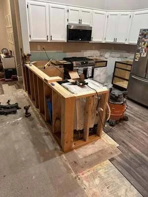 Kitchen island under renovation with white upper cabinets and wood base frame during construction phase