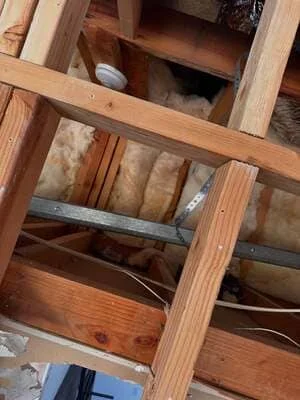 Attic insulation installation with fiberglass batts between wooden joists and framing
