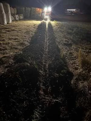 Excavated site at night with heavy equipment and work lights illuminating cleared ground